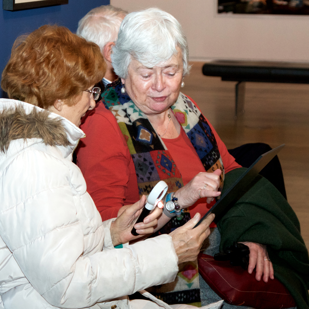 Two members of the Henshaws Group explore colour copies of artworks at a described tour of an exhibition at Gallery Oldham
