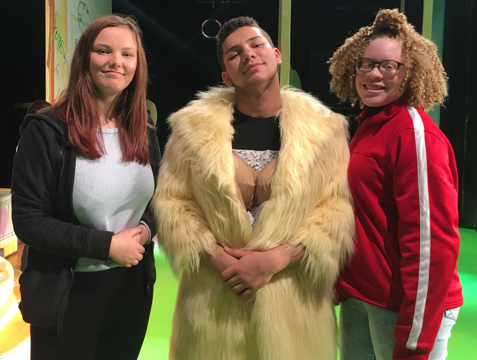 Three young partially sighted attenders at a touch tour for a pantomime at Oldham Coliseum Theatre. The lad is trying on the Dame's false boobs and fur coat